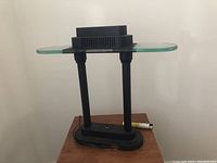 Front side view of a modernist black lamp with a rectangular glass shade and ventilation slits on the bulb housing.