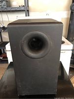 Front view of black subwoofer showing circular port opening.