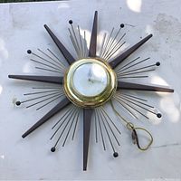 Close-up view of vintage starburst clock face and rays showing brass housing and wooden and metal decorative elements.