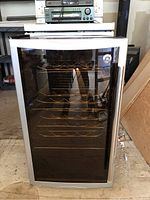 Closed view of GE wine and beer chiller showing stainless steel frame and tinted glass door with metal racks inside.