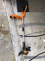 Single cordless garden trimmer/edger unit placed on a light-colored surface showing overall equipment and handle.