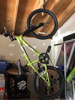 Full side view of the green youth bicycle hanging in a garage, showing frame, wheels, seat, pedals, and handlebar.