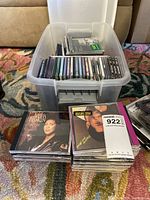 Plastic bin filled with CDs and two stacks of CDs placed in front, including an Aretha Franklin album.