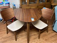 Angled front view of semi-circular walnut veneer table with two matching chairs.