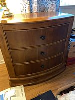 Front view of wooden nightstand showing curved front and three drawers with black knobs