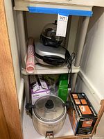 Photo of white utility shelf with kitchen appliances and boxed items including rice cooker, electric grill, and food chopper.