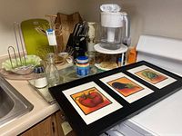 Kitchen counter with multiple kitchen items including framed wall art, blender, Brita pitcher, cutlery block, bowls, and can opener.