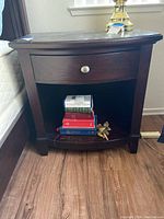 Front view of the wood nightstand showing the single drawer and open shelf with books and a figurine inside.