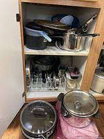 Full cabinet view showing various pots, pans, lids, bakeware racks, and containers arranged inside and a glass baking dish outside cabinet.