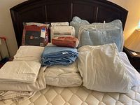 Queen bed headboard with various folded linens and packaged bedding on bed mattress