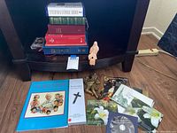 Lower shelf with religious pamphlets, CDs, and two light wood-colored cherub figurines on a dark wooden shelf.