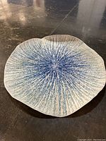 Full view of the scalloped round area rug with blue radiating speckled pattern on gray background.