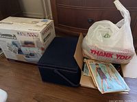 Photo showing collection of vintage sewing patterns in cardboard box, blue fabric-covered sewing box, and Kenmore sewing machine box.