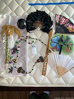 Top-down view of all souvenir items on a mattress showing the mask, fans, beads, percussion instrument, and umbrella.