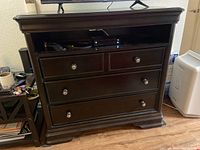 Front view of dark wood TV cabinet dresser, showing four drawers and an open shelf with a media device inside.