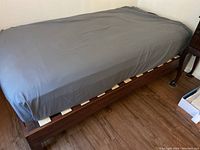 Twin wood platform bed frame with dark gray fitted sheet.