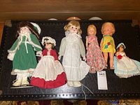 Wide shot of six vintage dolls placed side-by-side showing varied outfits and sizes.