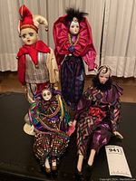 Four vintage Harlequin dolls displayed together on a black table in front of cream curtains, showing full outfits and faces.
