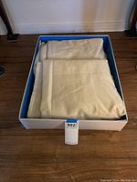 Cream-colored window curtains folded in a box, showing their texture and condition.