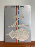 Full view of vintage poster showing architectural design of Montreal Olympic Stadium with rainbow stripe and Montreal 1976 print.