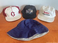 Four baseball caps and one reversible bucket hat arranged on a surface.