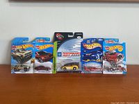 Six Hot Wheels 1:64 scale cars in original packaging, displayed side by side on wooden surface against beige wall
