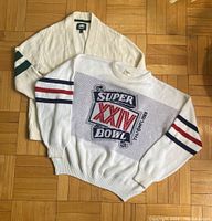 Both sweaters laid flat on wood parquet floor, showing front detail of knit Super Bowl XXIV sweater with stripes and graphic and cream Roots cardigan with stripes and logo.