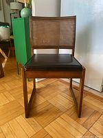 Front view of the mid century wooden chair with cane back and black seat cushion.