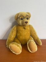 Full frontal view of the golden yellow mohair teddy bear wearing round metal glasses, seated upright against a white backdrop.