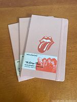 Three brand new Moleskine x The Rolling Stones ruled notebooks stacked with covers visible showing peach color and tongue logo.
