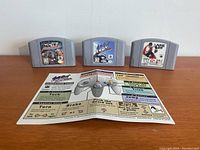 Three Nintendo 64 cartridges (WCW/NWO Revenge, 1080 Snowboarding, NHL 99) and 1080 Snowboarding instruction manual laid out on table