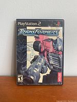 Front cover of Transformers PlayStation 2 game showing red Transformer character and Atari logo.