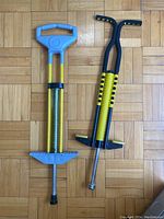 Both pogo sticks side by side on a wooden parquet floor showing distinct handle and footrest designs