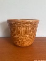 Front and side view of light brown ceramic vase with geometric and linear textured pattern around exterior, showing wide circular opening and shape.