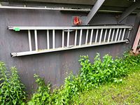 Full view of 20-foot aluminum extension ladder leaning against a wooden shed wall outdoors