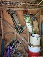 Four golf bags leaning against wooden wall, each with multiple golf clubs inside.