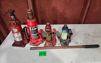 Four hydraulic jacks in varying condition: two 8 ton (red), two 2 ton (red and blue) with handle laid in front. Surfaces show wear, rust, and dirt.