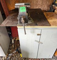 Full setup of the 6-inch swivel vise on steel plate and two-door metal storage stand in workshop environment, viewed from the front.