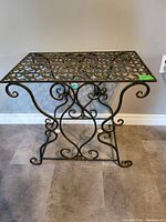Full view of metal accent table with ornate scrollwork design on top and curved legs.