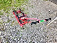 Red hydraulic jack on gravel with handle extended, showing base and lifting arms.