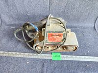 View of one Craftsman belt sander showing overall condition with wear, dirt, and power cord wrapped around