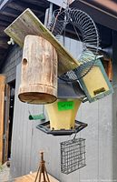 View of multiple hanging bird feeders including wooden suet feeder, peanut feeder, regular feeder, and small suet cage.
