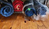 Rolled sleeping pads and sleeping bag along a rack, showing colors and condition including plastic wrapping.