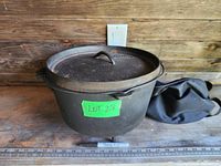 Large 12" cast iron pot with lid, handle, and black storage bag displayed on wood shelf with measuring tape for scale.