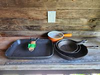 Full view of all items showing three cast iron pans, orange pot, and folding skillet