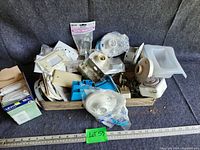 Wide view of boxed electrical supplies showing metal boxes, plastic wall plates, timer, and other small hardware pieces inside a wooden tray.