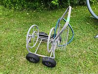 Full view of the garden hose reel cart on grass showing metal frame, four tires, and accessory basket.
