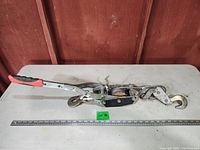 Top view of large come along hand winch with red rubber grip handle and steel cable.