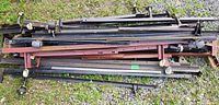 Large collection of black and red painted steel beams and bars lying outdoors on gravel, with attached mounting brackets and adjustable hardware.