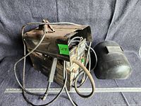 Front and side view of MIG welder with attached welding torch and cables. Shows wear, dirt, and condition of the unit. Green label sticker visible.